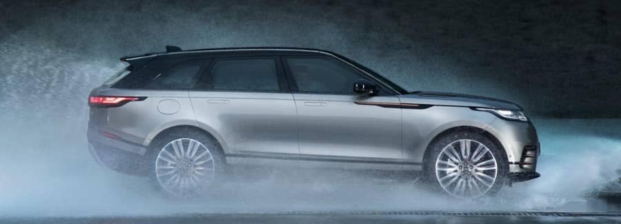 2022rangerover_velar-sideview-driving-through-puddle-huge-spray-dark grey-background-silver
