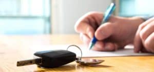 Persons hand signing off on car loan with car keys in the picture frame