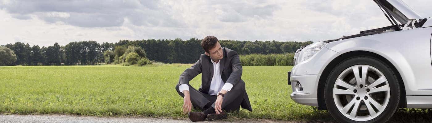 Man Sitting Beside Overheating Car