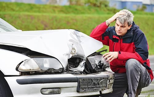 Man crouched over his front bumper damage looking upset