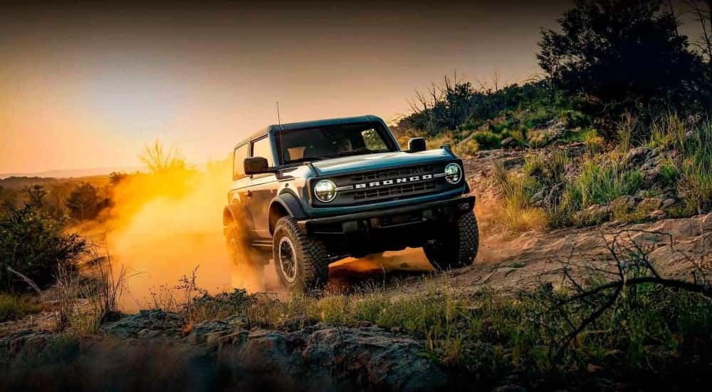 A blue 2022 Ford Bronco is shown kicking up dust off-road.