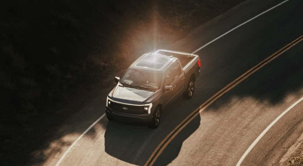A grey 2023 Ford F-150 Lightning is shown driving to a Ford Lightning dealer.
