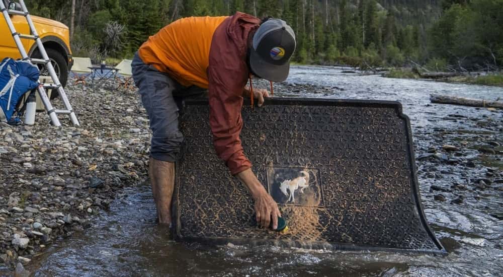 A person is shown washing a floor mat near a yellow 2021 Ford Bronco Sport Badlands.