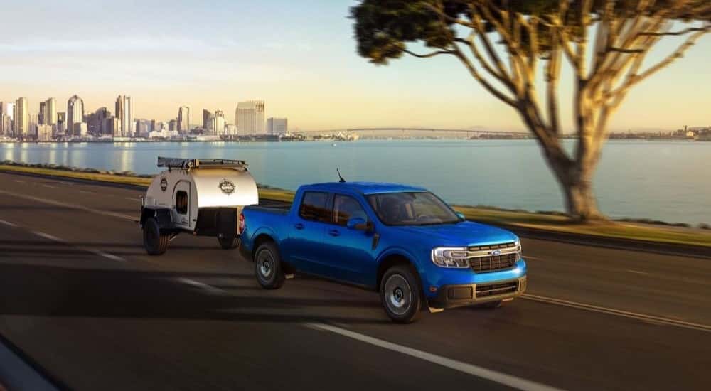 A blue 2023 Ford Maverick is shown towing a small trailer after leaving a Conyers Ford dealer.