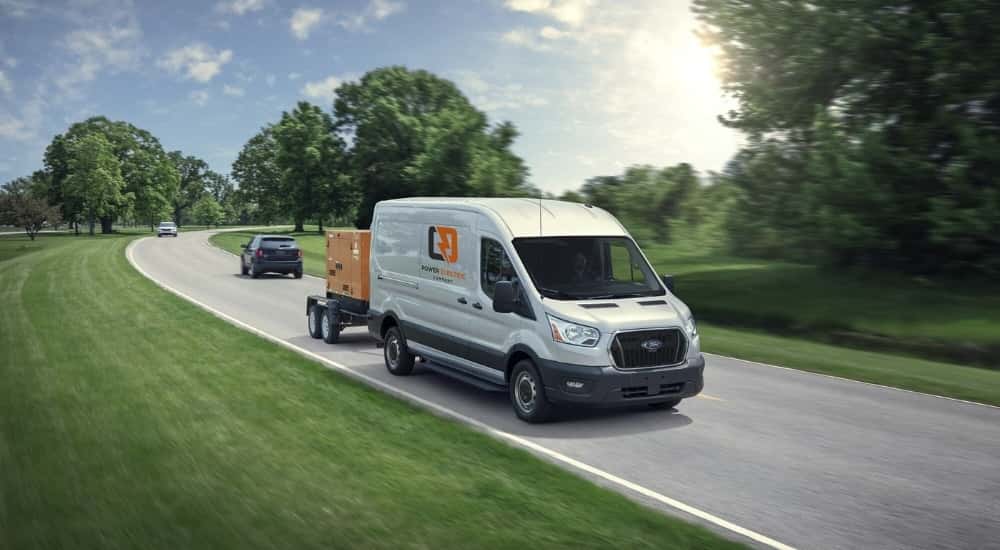 A white 2023 Ford Transit is shown towing power equipment on a highway.