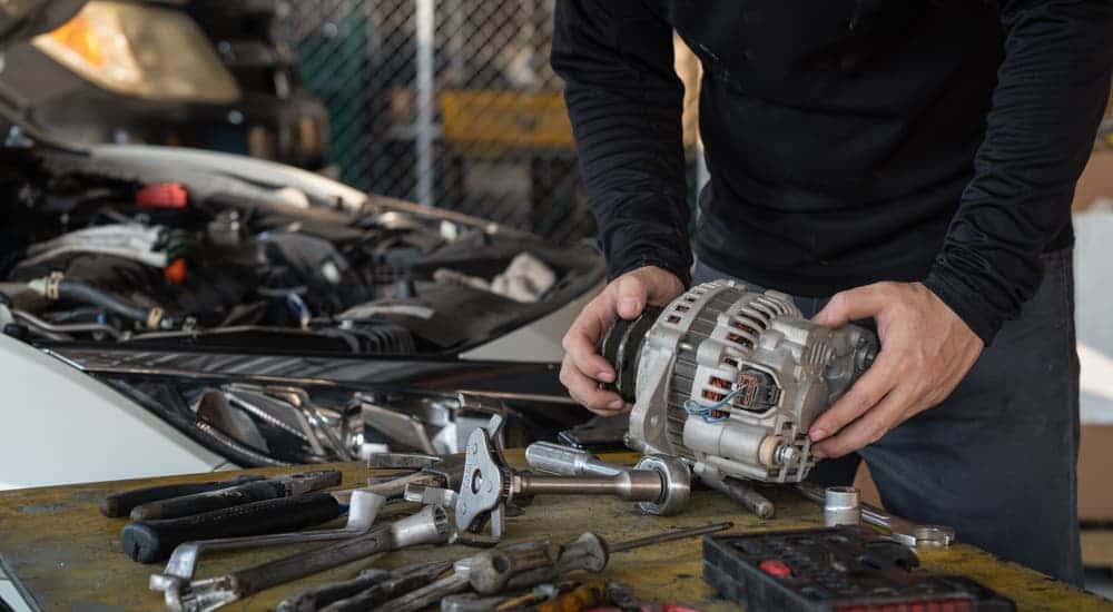 A mechanic holding an alternator over a workbench.
