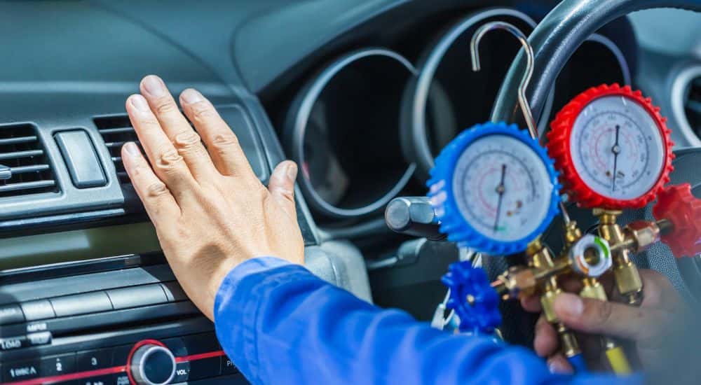 A mechanic reaching out to feel for air blowing while testing the AC system in a car.