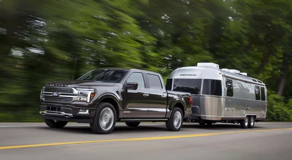 A grey 2024 Ford F-150 Platinum is shown towing a silver trailer after leaving a Ford dealer near Forest Park.