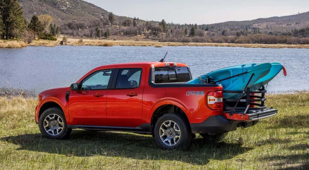A red 2024 Ford Maverick FX4 with kayaks in the bed parked by water.