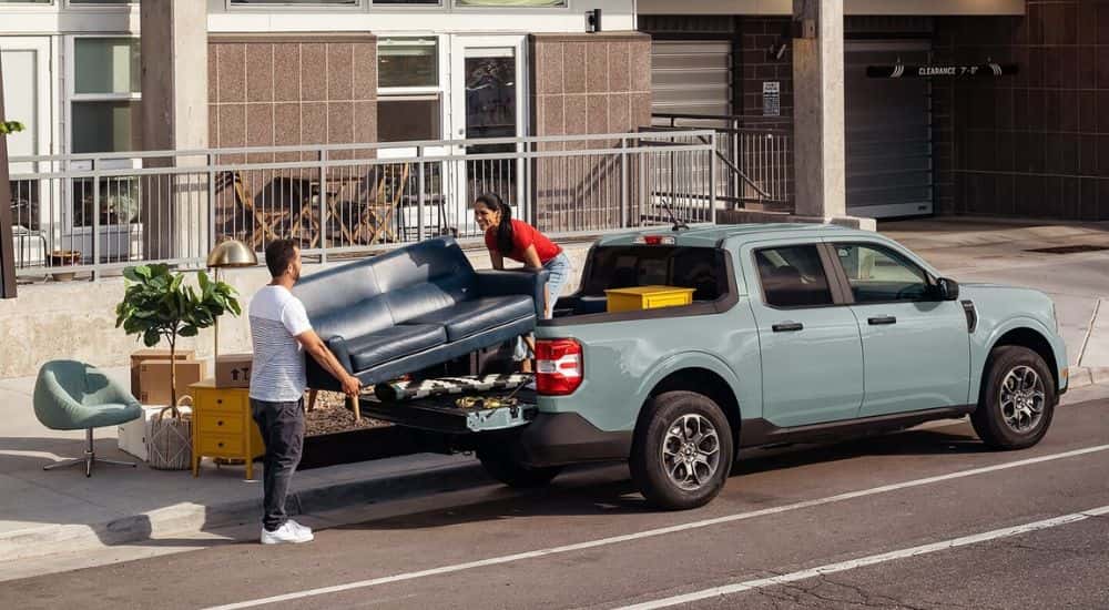 A couple loading furniture into the bed of a light blue 2024 Ford Maverick.