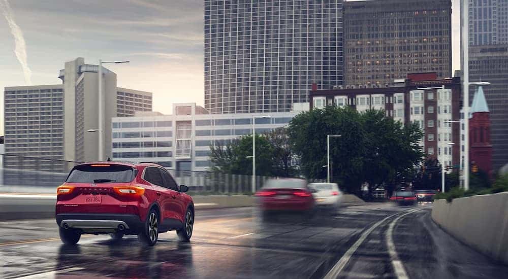 A red 2024 Ford Escape Platinum driving on a city street during a rainstorm.