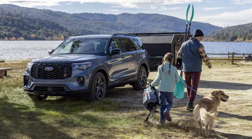 A family is walking near a blue 2025 Ford Explorer ST parked on a campsite near a lake.