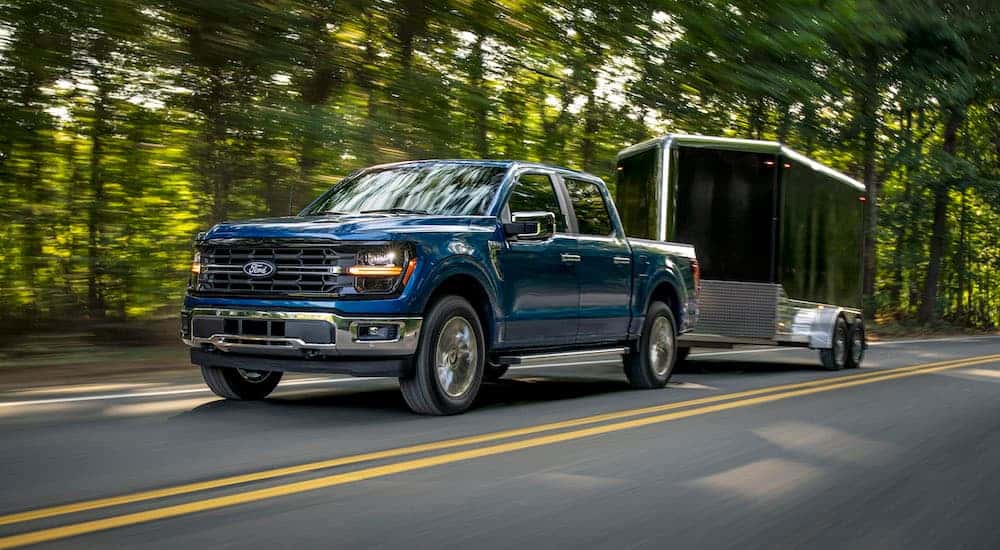 A blue 2025 Ford F-150 is shown from the front at an angle while towing a trailer.