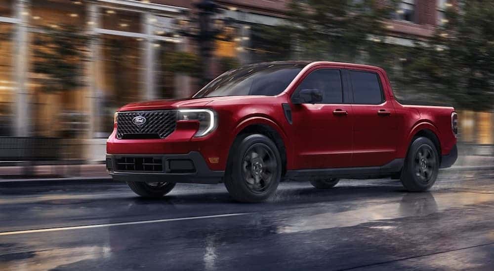 A red 2025 Ford Maverick driving through a rainy city from a Ford dealer near Stone Mountain.