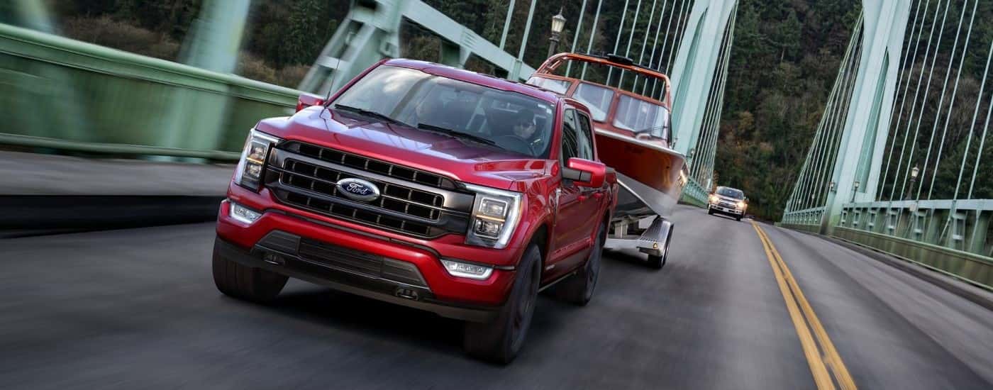 A red 2023 Ford F-150 Hybrid is shown driving over a bridge while towing a boat.