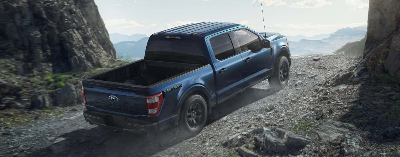 A dark blue 2023 Ford F-150 Rattler is shown from a rear angle driving out a mountain trail.