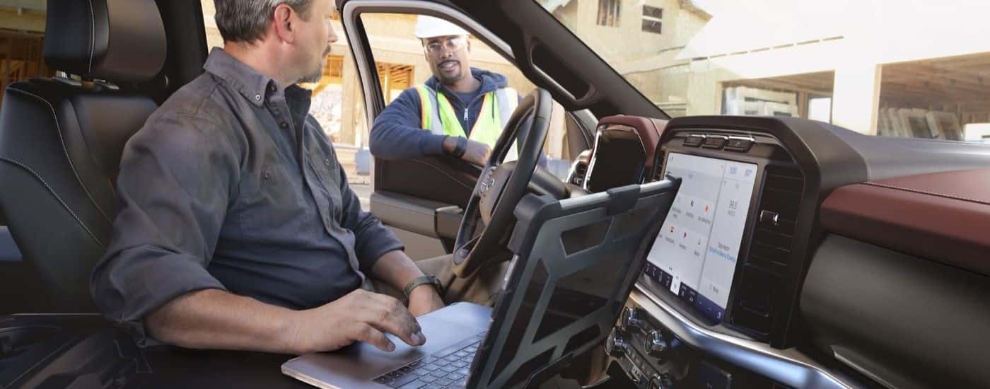 A person is shown using a laptop in a 2023 Ford F-150 on a construction site.