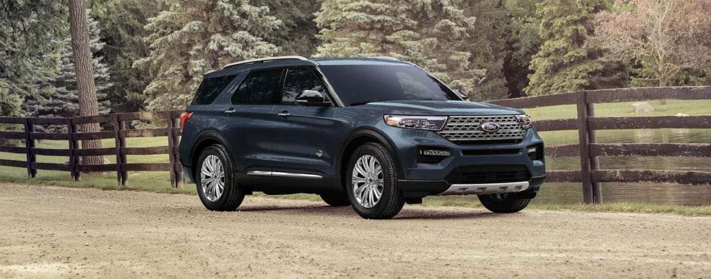 A turquoise 2023 Ford Explorer is shown from the side parked in front of a wooden fence.