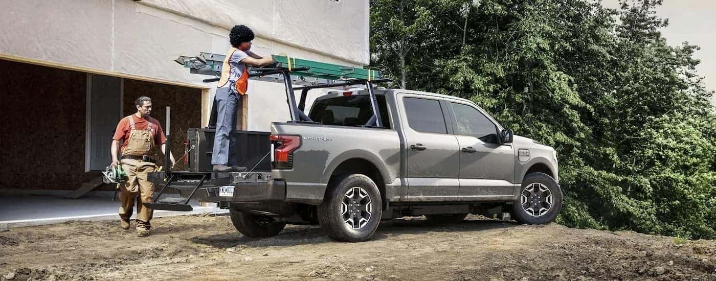 Two people are shown putting a ladder on a rack on a silver 2023 Ford F-150 Lightning.