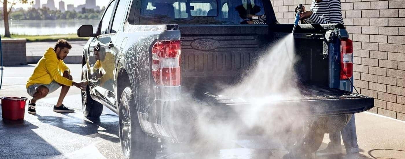 Two people are showing cleaning a grey 2023 Ford Maverick in a carwash bay.