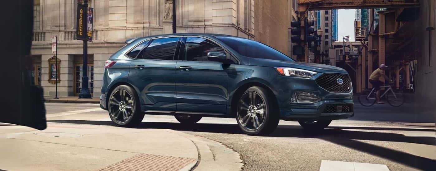 A blue 2024 Ford Edge ST is shown turning on a city street corner.