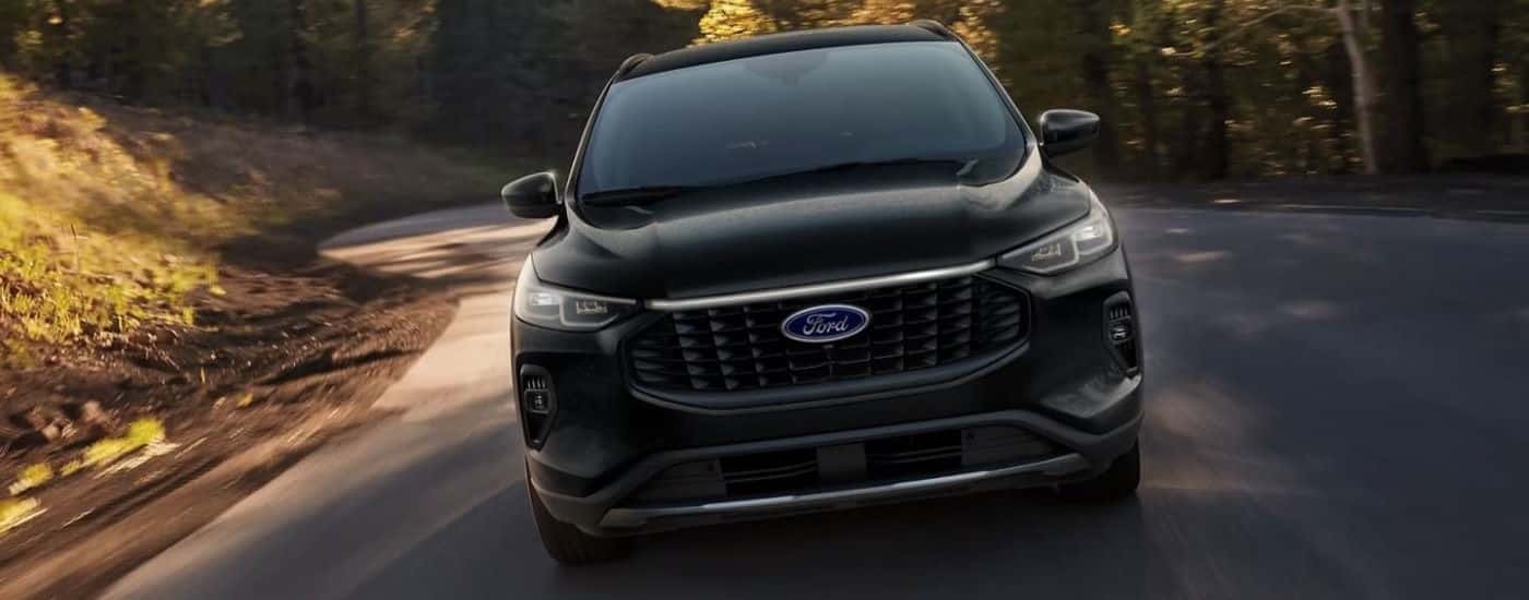 A black 2024 Ford Escape is shown from the front driving on a winding road.