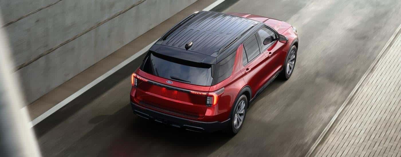 A red 2025 Ford Explorer for sale is driving on a highway during a test drive.