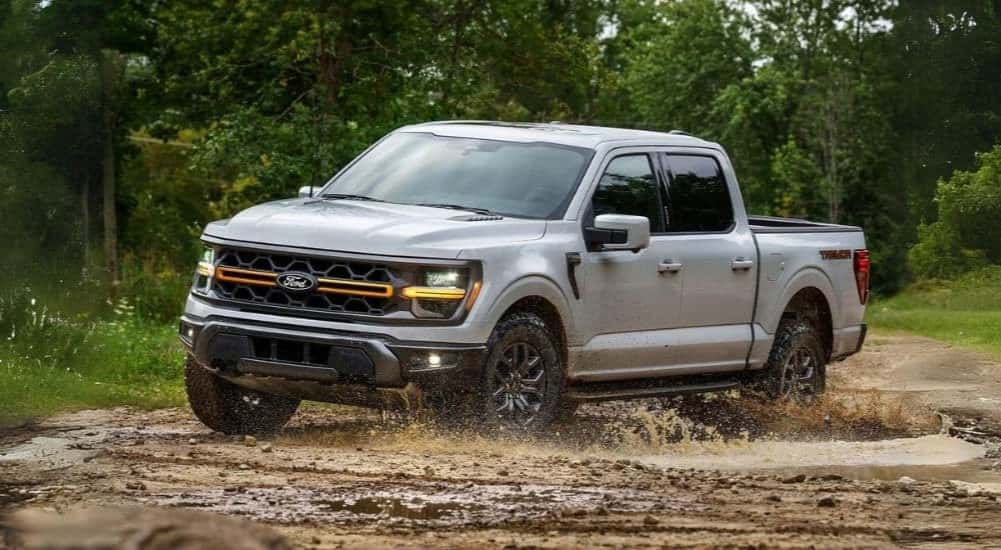A silver 2024 Ford F-150 Tremor is shown driving through mud.