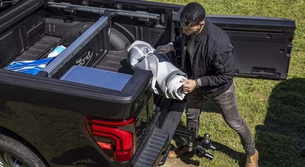 A person is shown unloading gear from the bed of a black 2024 Ford F-150.