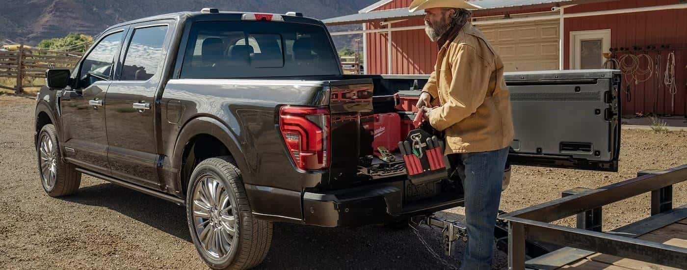 A farmer is shown putting supplies into the bed of a black 2024 Ford F-150 hooked up to a trailer.