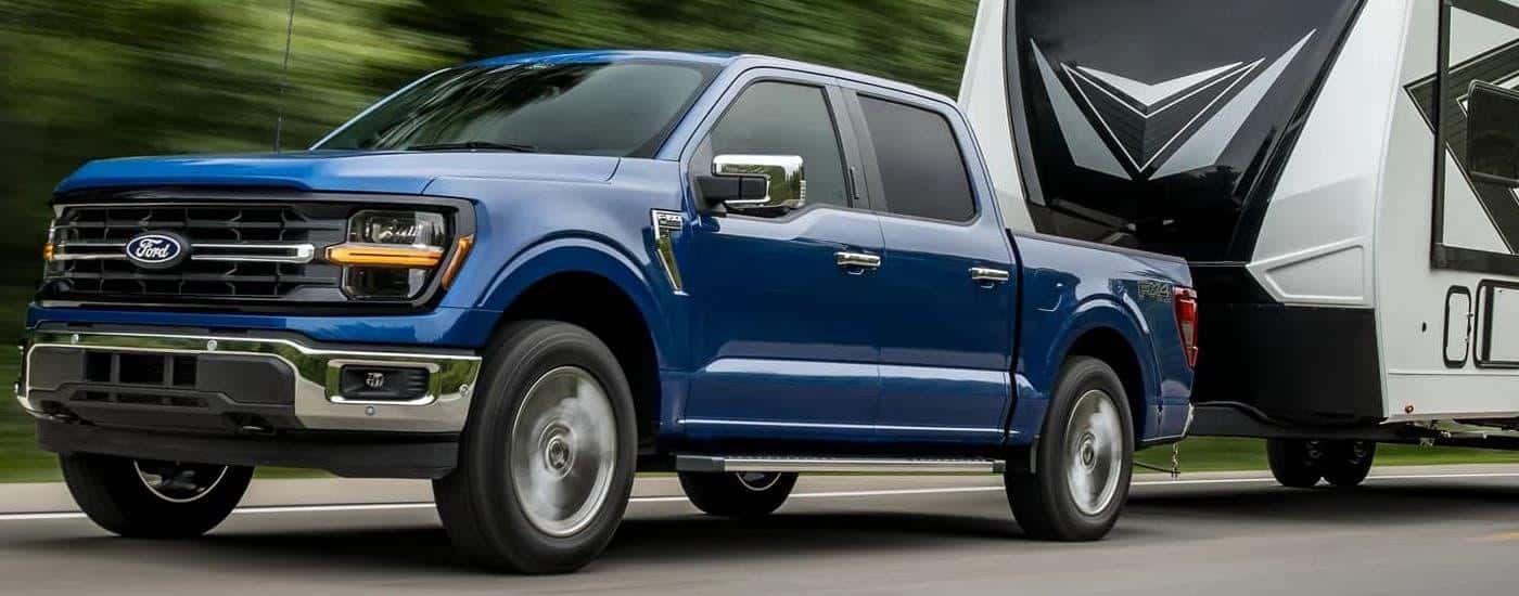 A blue 2024 Ford F-150 STX is towing a camper trailer.