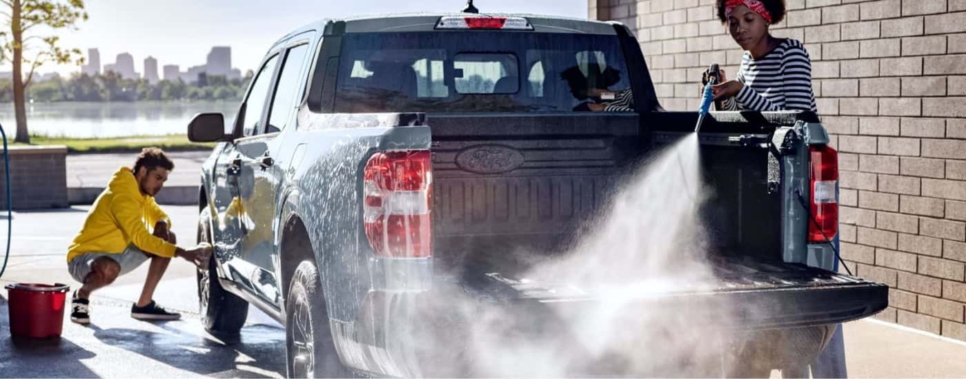 Two people are shown cleaning a 2024 Ford Maverick in a car wash bay.