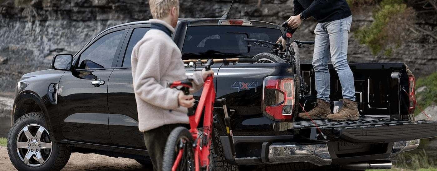 Two people are shown putting mountain bicycles into the bed of a black 2024 Ford Ranger.