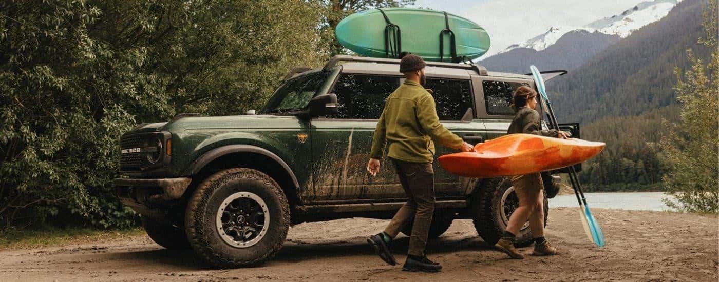 A green 2025 Ford Bronco Badlands is parked at a campsite with kayaks.