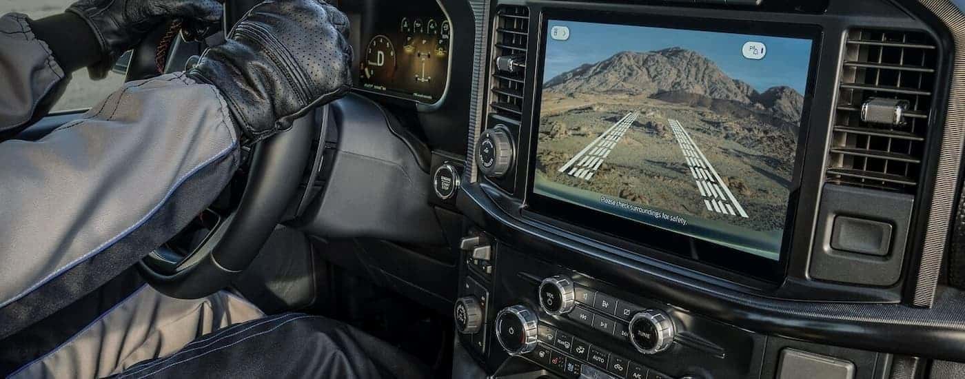 A close up of a person driving a 2025 Ford F-150 with the backup camera showing on the infotainment screen.