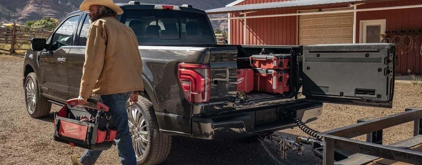 A man is walking next to a black 2025 Ford F-150 parked on a farm while hooked up to a trailer.
