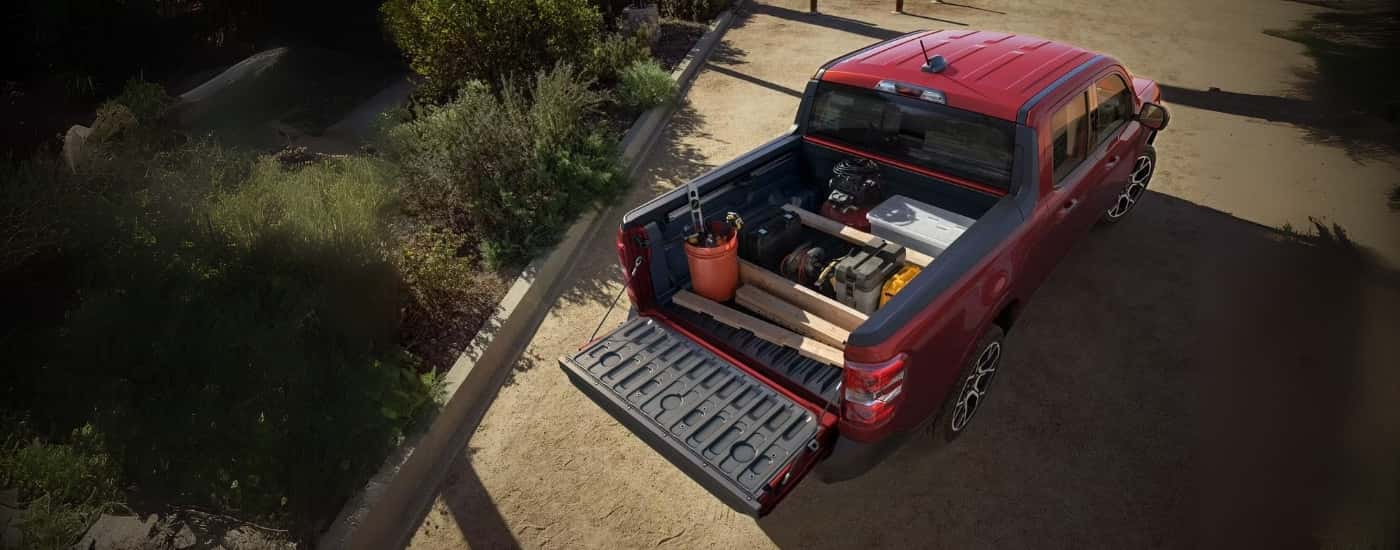 A red 2025 Ford Maverick Lariat is parked with a bed full of construction supplies.