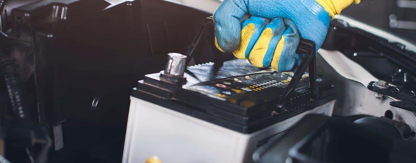 A close up of a mechanic putting a battery in a vehicle during an auto repair near Monroe.