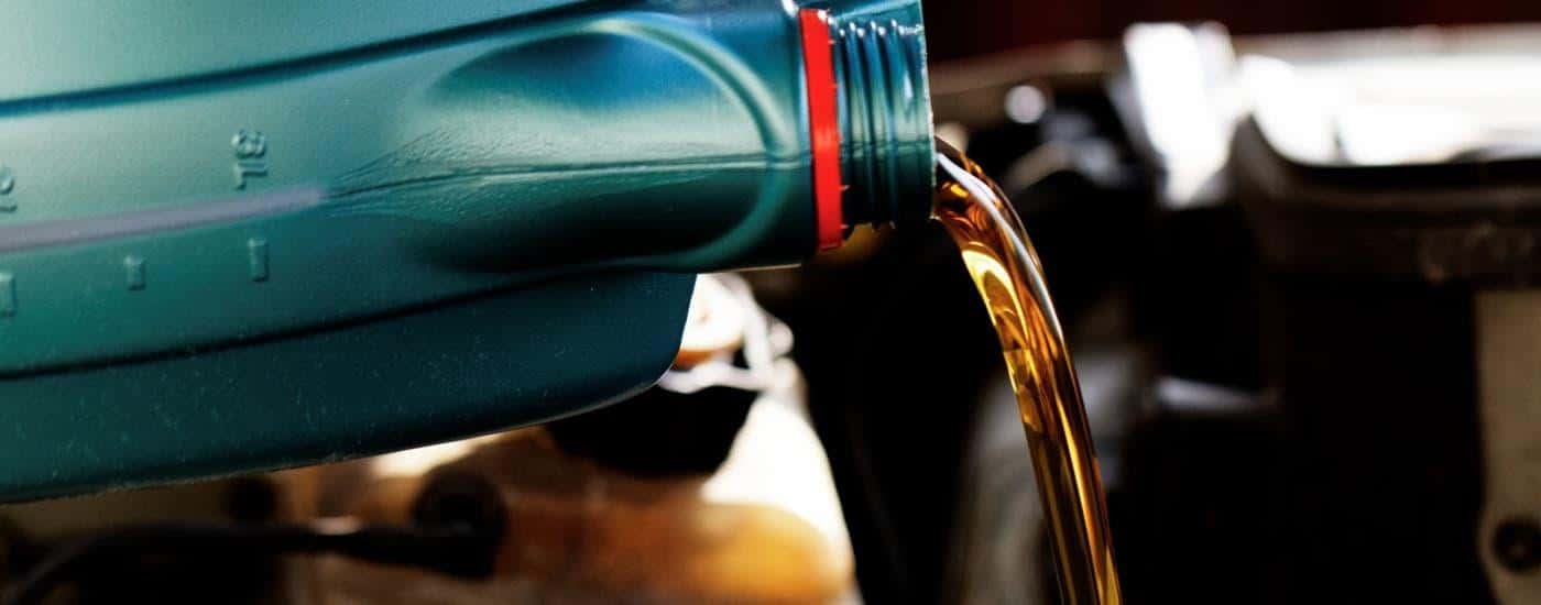 Oil is being poured out of a bottle and into a vehicle's engine.