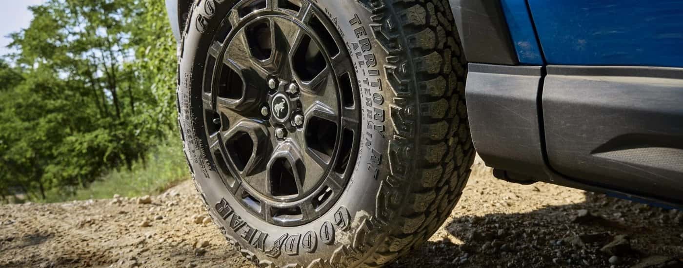 A close-up shows a black wheel on a blue 2025 Ford Bronco Sport.