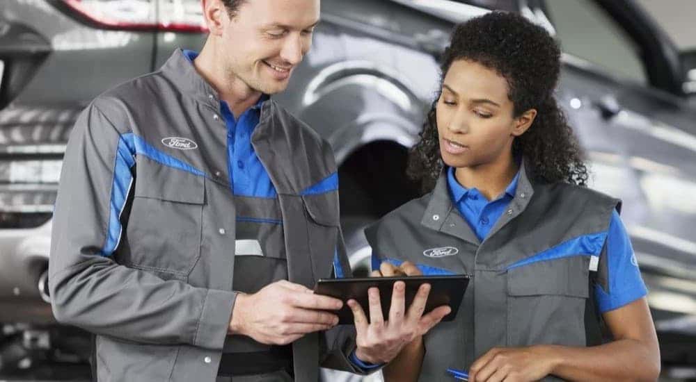 Ford technicians are shown near a vehicle on a lift at an auto repair shop.