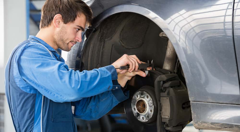 A mechanic performing brake service on a silver vehicle.