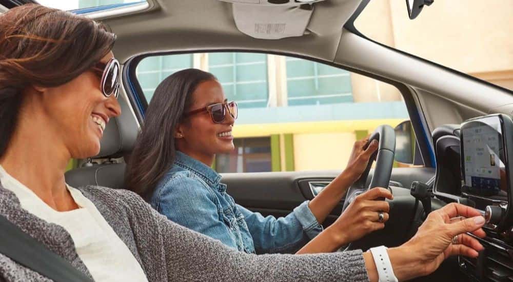 Two smiling women driving in a 2021 Ford EcoSport after getting engine repairs done.