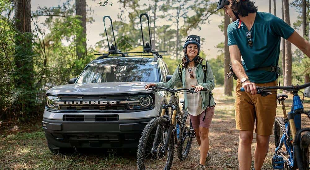 Two people with bikes are walking away from a white 2023 Ford Bronco Sport.