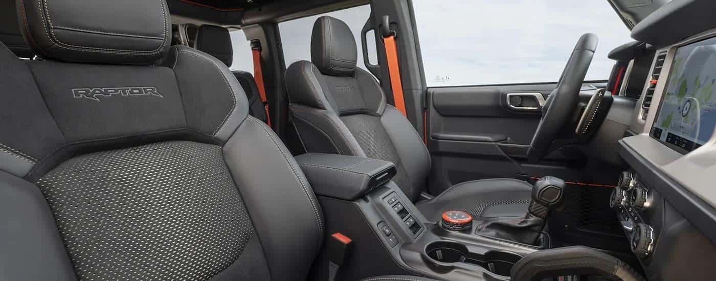 The grey and orange interior of a 2023 Ford Bronco Raptor shows the front seats and center console.
