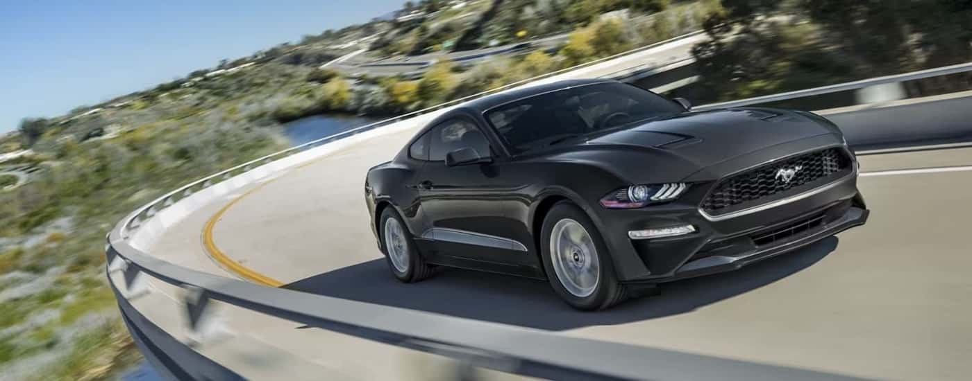 A grey 2023 Ford Mustang Ecoboost Fastback is shown driving on a winding highway during a test drive at a Ford dealer.