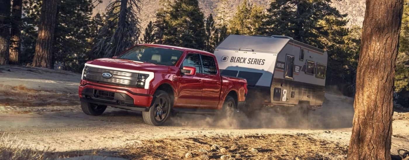 A red 2022 Ford F-150 Lightning is shown towing a closed trailer on a dirt road.
