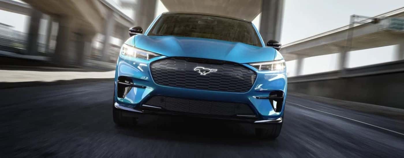 A blue 2021 Ford Mustang Mach-E is shown driving on an open road.
