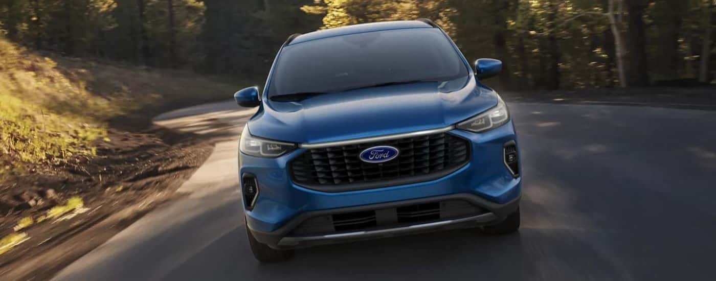 A blue 2023 Ford Escape is shown from the front driving on a winding road.