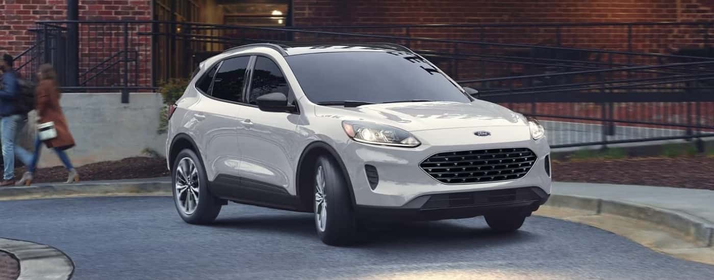 A white 2022 Ford Escape is shown from the front driving past a brick building.